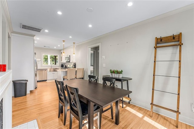 dining area with sink, ornamental molding, and light wood-type flooring