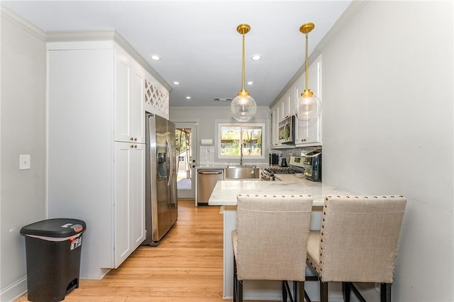 kitchen with white cabinetry, sink, stainless steel appliances, kitchen peninsula, and a breakfast bar area