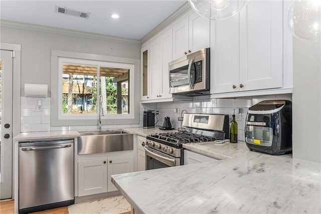 kitchen featuring white cabinets, appliances with stainless steel finishes, light stone counters, and sink