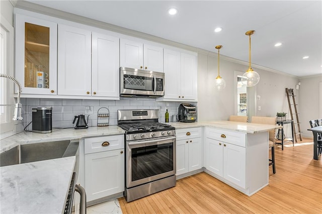 kitchen featuring kitchen peninsula, white cabinetry, decorative light fixtures, and appliances with stainless steel finishes