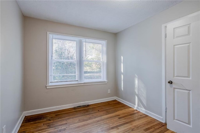 empty room with hardwood / wood-style flooring, visible vents, and baseboards