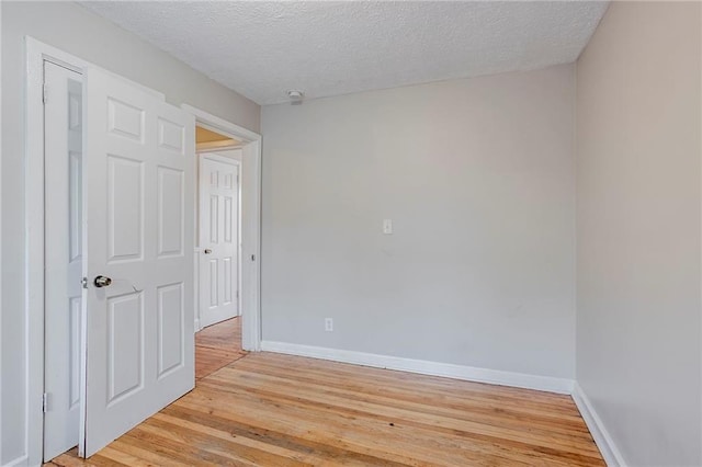 empty room with light wood finished floors, baseboards, and a textured ceiling