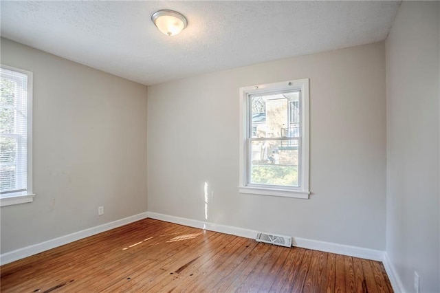 spare room featuring hardwood / wood-style flooring, baseboards, visible vents, and a textured ceiling