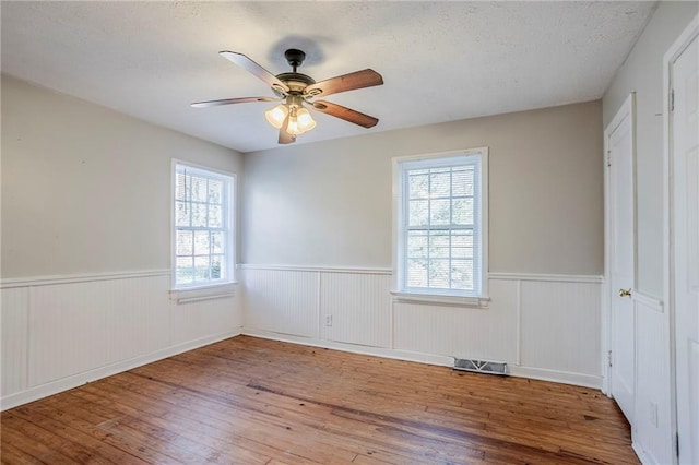 unfurnished bedroom with hardwood / wood-style floors, multiple windows, wainscoting, and visible vents