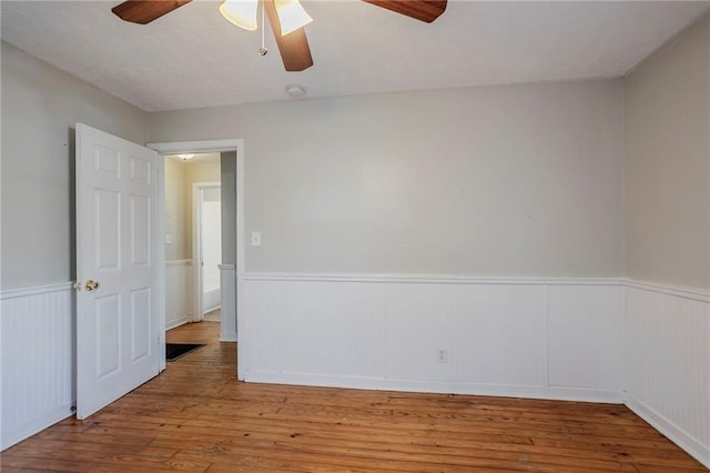 spare room with a ceiling fan, wood finished floors, and wainscoting