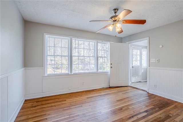 unfurnished room with a wainscoted wall, a textured ceiling, a ceiling fan, and hardwood / wood-style flooring