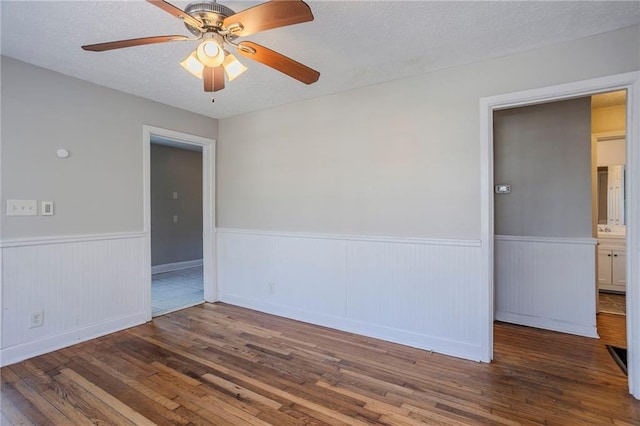 empty room with a wainscoted wall, a textured ceiling, hardwood / wood-style flooring, and a ceiling fan