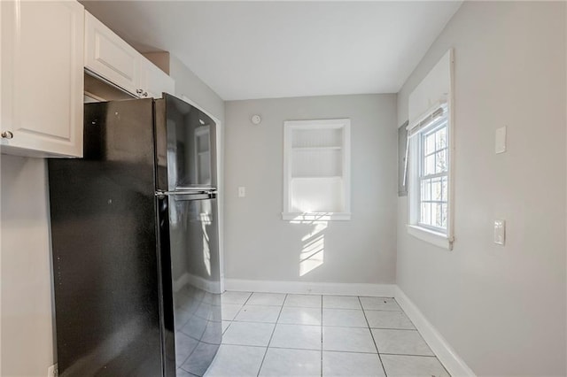 kitchen with freestanding refrigerator, white cabinetry, baseboards, and light tile patterned flooring