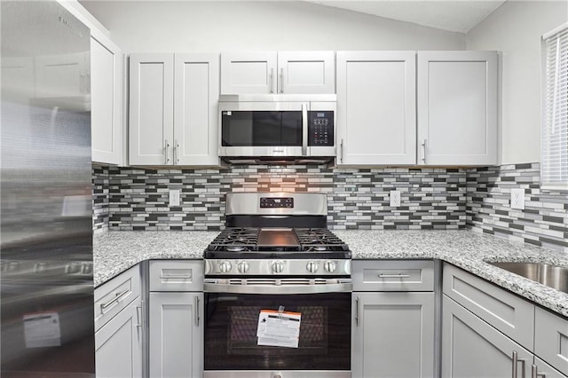 kitchen featuring appliances with stainless steel finishes, tasteful backsplash, light stone counters, gray cabinetry, and vaulted ceiling