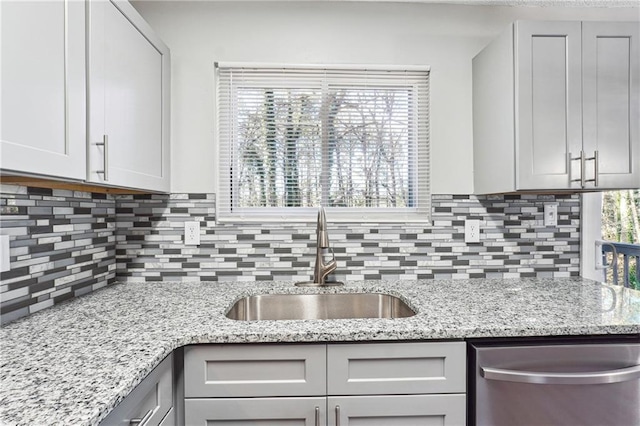 kitchen with dishwasher, backsplash, light stone counters, and sink