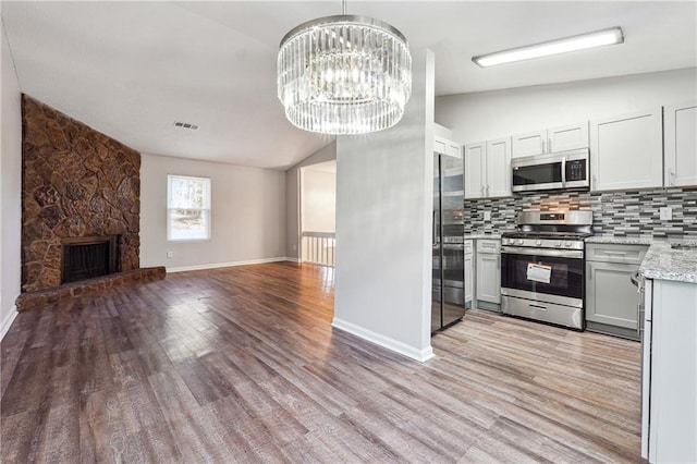 kitchen featuring lofted ceiling, backsplash, a stone fireplace, stainless steel appliances, and a chandelier