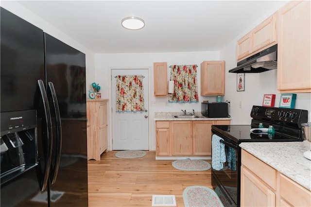 kitchen with light stone countertops, black appliances, light brown cabinets, sink, and light hardwood / wood-style flooring