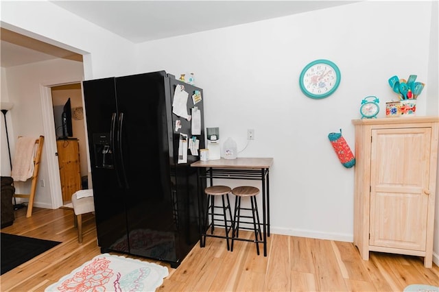 interior space with a kitchen breakfast bar, light wood-type flooring, and black fridge with ice dispenser