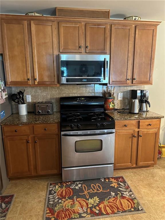 7946 Gossamer, Fairburn, GA 30213 - kitchen featuring appliances with stainless steel finishes, backsplash, dark stone counters, and brown cabinetry