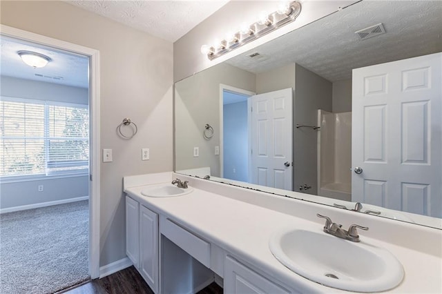 bathroom featuring vanity, wood-type flooring, a shower, and a textured ceiling