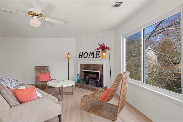 living room featuring visible vents, a ceiling fan, wood finished floors, baseboards, and a brick fireplace