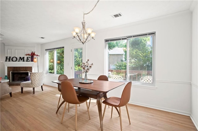 dining space with visible vents, light wood-style floors, an inviting chandelier, a fireplace, and crown molding