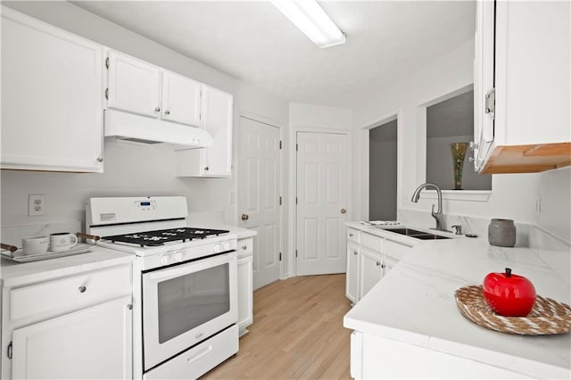 kitchen featuring white range with gas cooktop, white cabinets, under cabinet range hood, and a sink