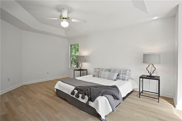 bedroom featuring a tray ceiling, baseboards, light wood-style flooring, and a ceiling fan