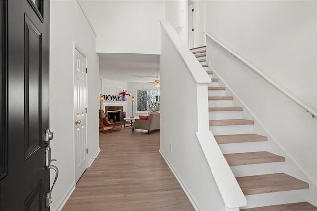 foyer entrance with stairway, baseboards, a fireplace, and light wood finished floors