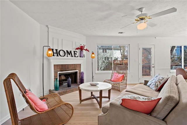 living area with a brick fireplace, a textured ceiling, light wood-type flooring, and a ceiling fan