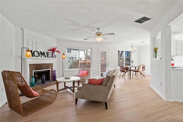 living area featuring visible vents, light wood-style flooring, a fireplace, a textured ceiling, and ceiling fan with notable chandelier