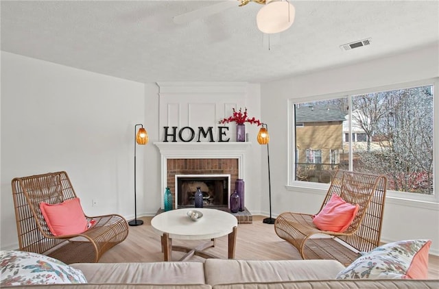 living area featuring visible vents, a ceiling fan, wood finished floors, a fireplace, and baseboards