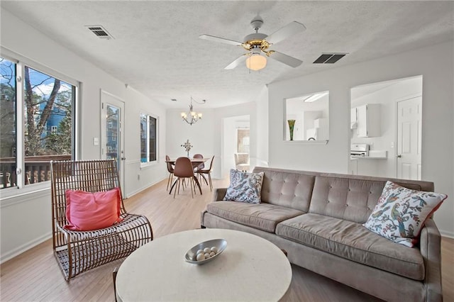 living area with visible vents, a textured ceiling, light wood-style flooring, and ceiling fan with notable chandelier