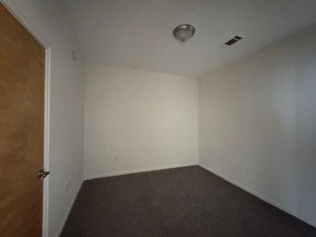 empty room featuring visible vents, baseboards, and dark colored carpet