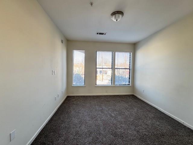 empty room with dark colored carpet, visible vents, and baseboards