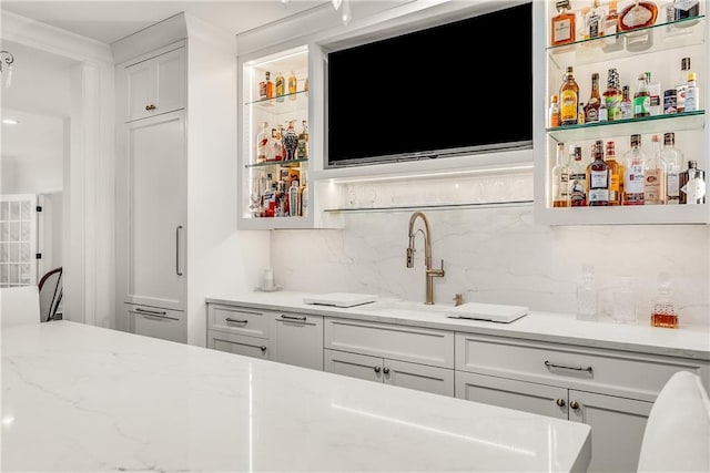 bar featuring light stone counters, sink, decorative backsplash, and white cabinets