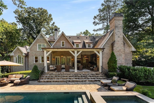 rear view of property with a swimming pool with hot tub, an outdoor living space with a fire pit, and a patio