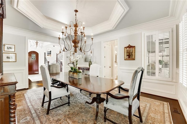 dining area with hardwood / wood-style flooring, ornamental molding, a raised ceiling, and a chandelier