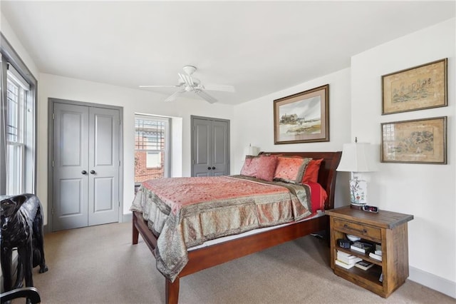 bedroom featuring light carpet, ceiling fan, and multiple closets