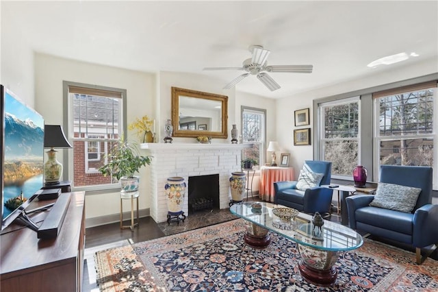 living room featuring a ceiling fan, a fireplace, baseboards, and wood finished floors