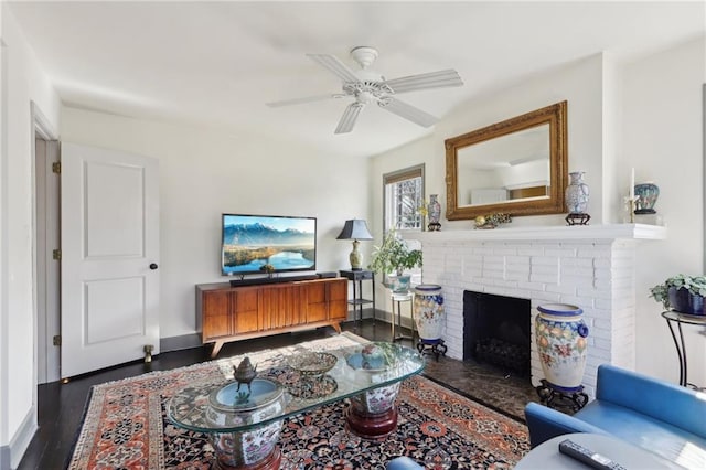 living area featuring dark wood-style floors, ceiling fan, a brick fireplace, and baseboards