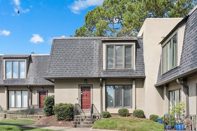 townhome / multi-family property featuring a shingled roof, mansard roof, and stucco siding