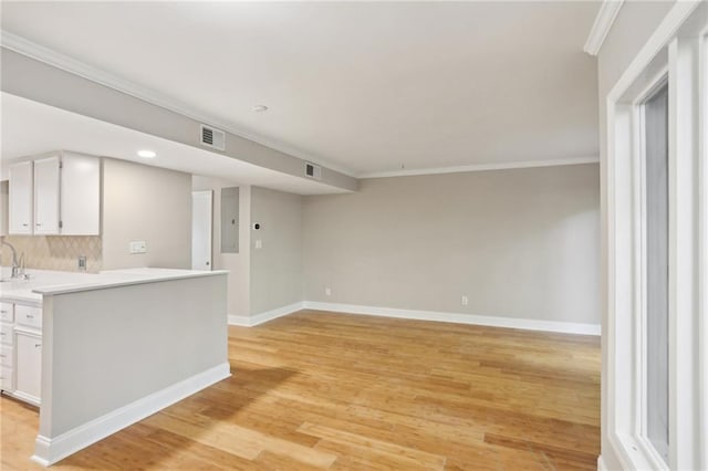 kitchen with baseboards, light countertops, ornamental molding, and white cabinets