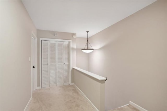 hall featuring light carpet, baseboards, and an upstairs landing