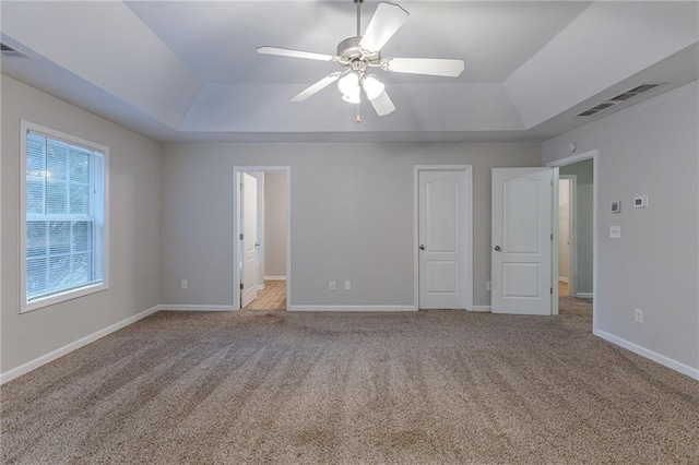 unfurnished bedroom with ceiling fan, ensuite bath, light carpet, and a tray ceiling