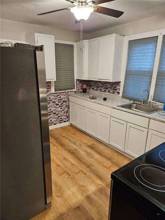 kitchen with sink, light wood-type flooring, stainless steel refrigerator, black range with electric cooktop, and white cabinets