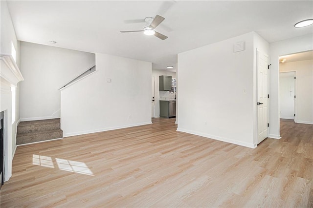 unfurnished living room featuring a fireplace, a ceiling fan, baseboards, stairs, and light wood-style floors