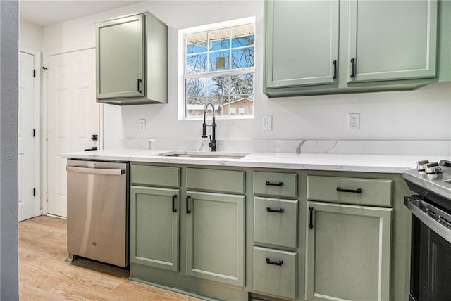 kitchen with appliances with stainless steel finishes, light wood-type flooring, a sink, and green cabinetry