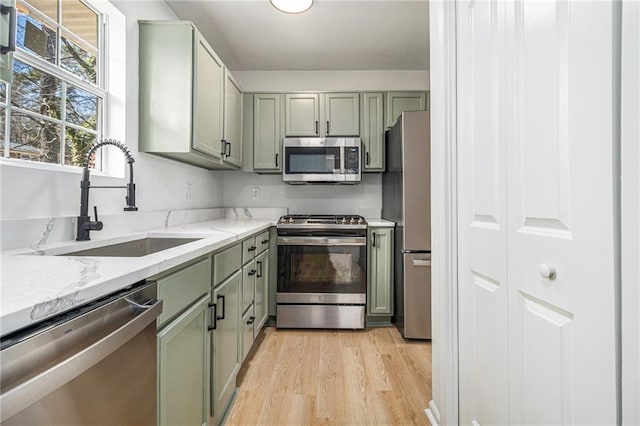 kitchen with light stone counters, light wood finished floors, stainless steel appliances, a sink, and green cabinetry