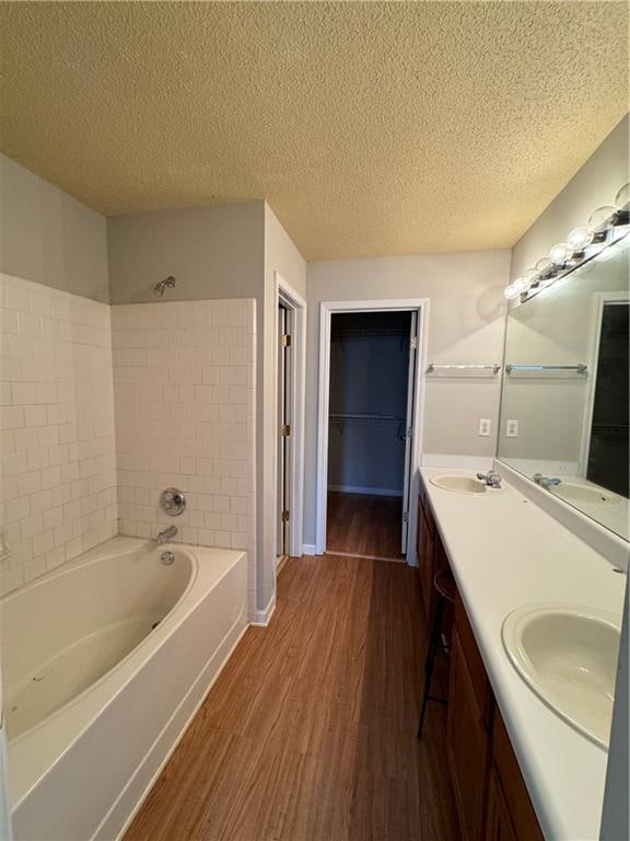 bathroom featuring tiled shower / bath combo, a textured ceiling, hardwood / wood-style flooring, and dual bowl vanity