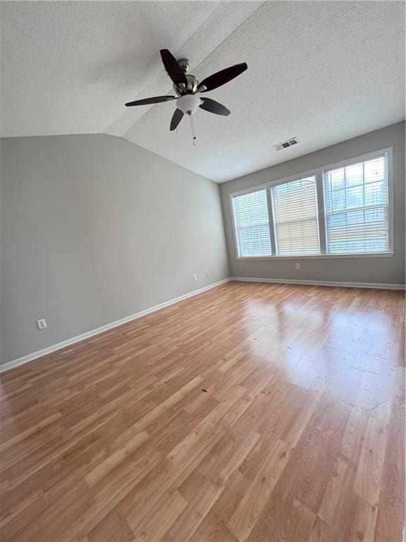 empty room featuring lofted ceiling, a textured ceiling, light hardwood / wood-style flooring, and ceiling fan