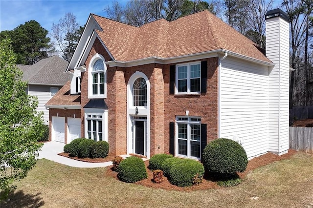 traditional-style home with a front lawn, fence, a garage, and roof with shingles