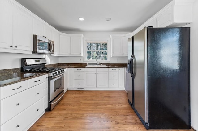 kitchen with dark stone countertops, stainless steel appliances, sink, and white cabinets