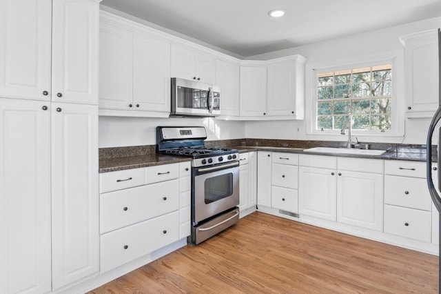 kitchen featuring sink, appliances with stainless steel finishes, dark stone countertops, light hardwood / wood-style floors, and white cabinets