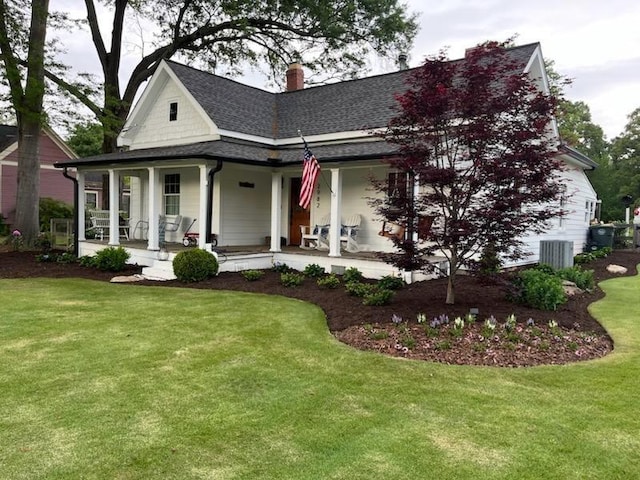 country-style home featuring covered porch, a front lawn, a chimney, and a shingled roof